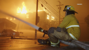 Firefighter sitting on a hose, water down an active fire.